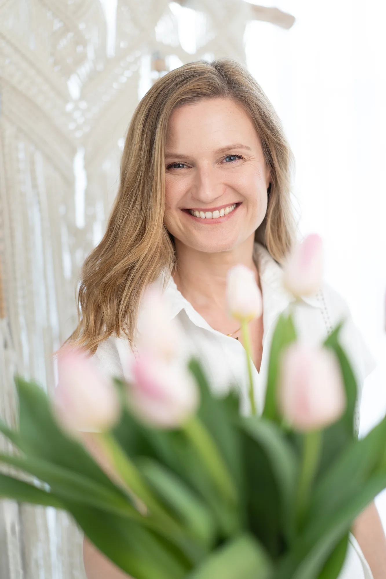 Joanna Radek-Petersen uśmiechnięta za bukietem jasnoróżowych tulipanów.